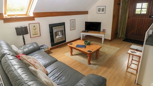 Una sala de estar con un sofá de cuero, una chimenea, un televisor sobre una mesa de madera y una ventana con cortinas.