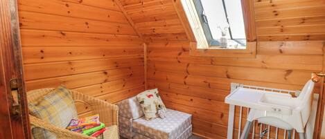 Une chambre mansardée chaleureuse avec des murs en bois, une petite fenêtre, un berceau, une chaise en osier et une table de chevet.