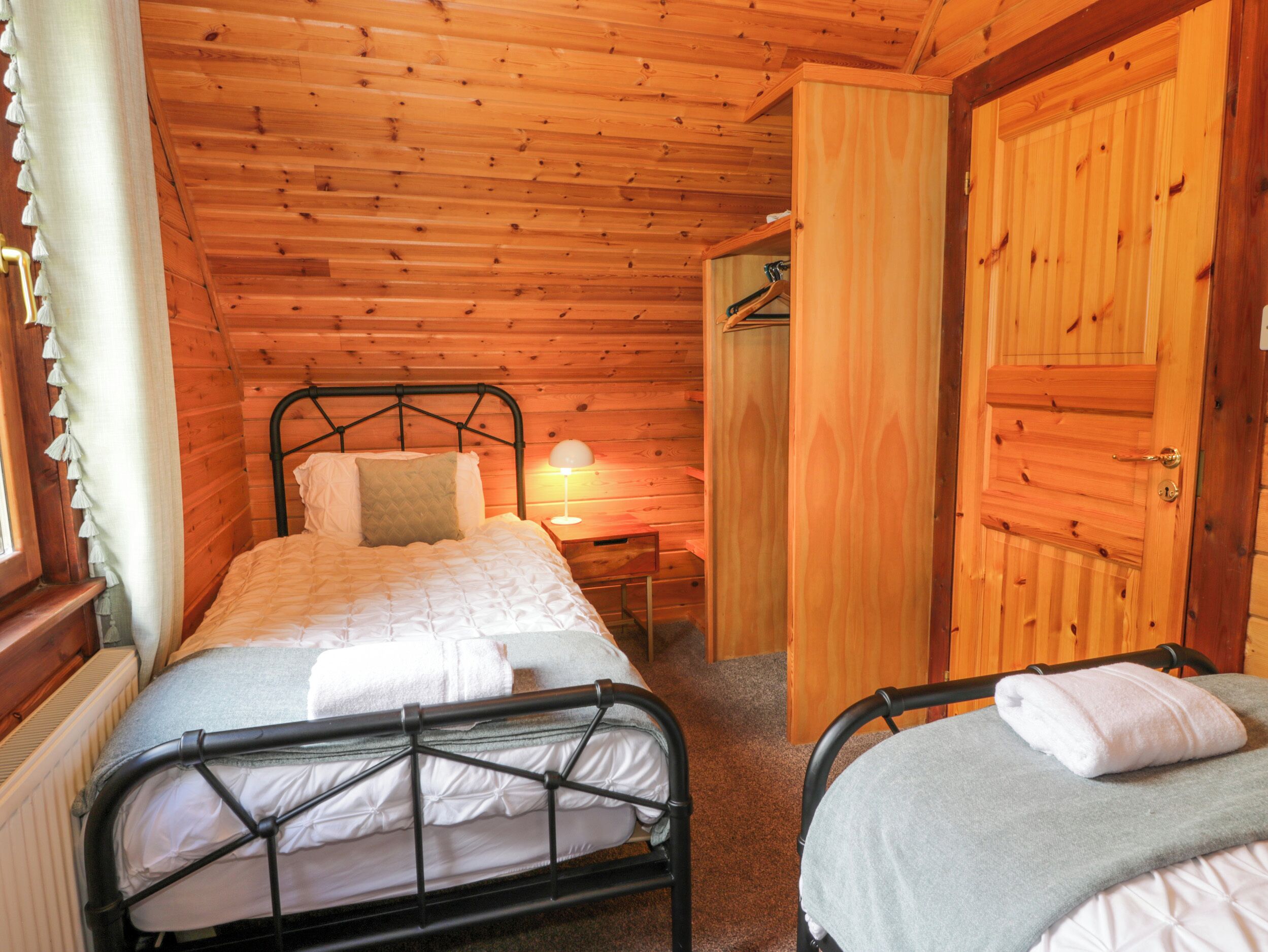Un dormitorio de cabaña de madera acogedor, con una cama individual, otra cama, una mesita de noche, una lámpara y un armario.
