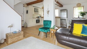 A spacious living area with a brown leather sofa, a teal armchair, and a wooden coffee table. A kitchen is visible in the background with a refrigerator and a dining table. - 220 Cae Du (Pwllheli)