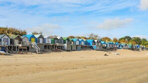 A row of beach huts with wooden staircases leading to the beach, under a clear sky. - 220 Cae Du (Pwllheli)