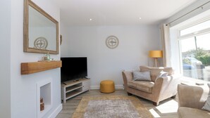 A living room with a television, a sofa, a lamp, and a large window. - Llwyn Eithin (Tyn-y-Gongl)