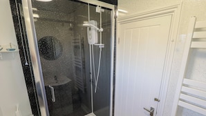 A modern bathroom with a glass-enclosed shower, a white door, and a small shelf with toiletries.