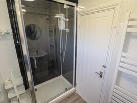 Un baño moderno con ducha separada por mampara de vidrio, una puerta blanca y un estante pequeño con artículos de aseo.