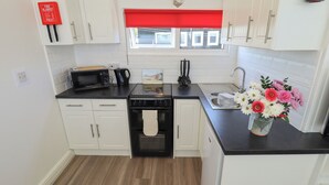 A modern kitchen with white cabinets, a black countertop, a stove, a microwave, and a sink. There is a fire blanket mounted on the wall and a vase with flowers on the countertop.