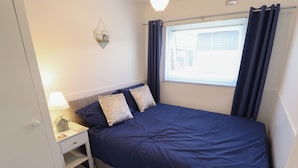 A bedroom with a bed, nightstand, lamp, and a window with curtains.