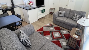 A compact living space with a kitchenette, grey sofa set, and a patterned rug.