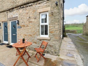 A stone building with a patio table and chairs, a bottle of champagne, and a glass.