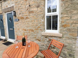 Un bâtiment en pierre avec une table ronde en bois et deux chaises, une bouteille de champagne et deux verres à vin.