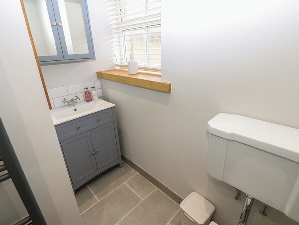 Une salle de bain avec un lavabo blanc, des meubles gris, une étagère en bois et des toilettes blanches.