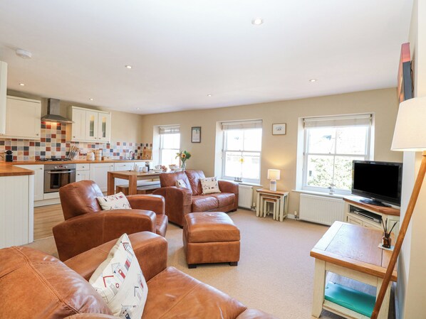 A modern living room with leather sofas, a dining area, a kitchen, and a TV. - Crab Corner (Wells-next-the-Sea)