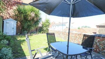 A patio with a table and chairs, a large umbrella, and a garden with a shed and plants.