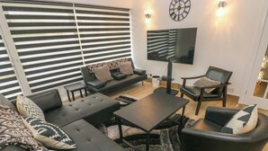 Een moderne woonkamer met een bank, salontafel en fauteuils, een flatscreen televisie en een wandklok.