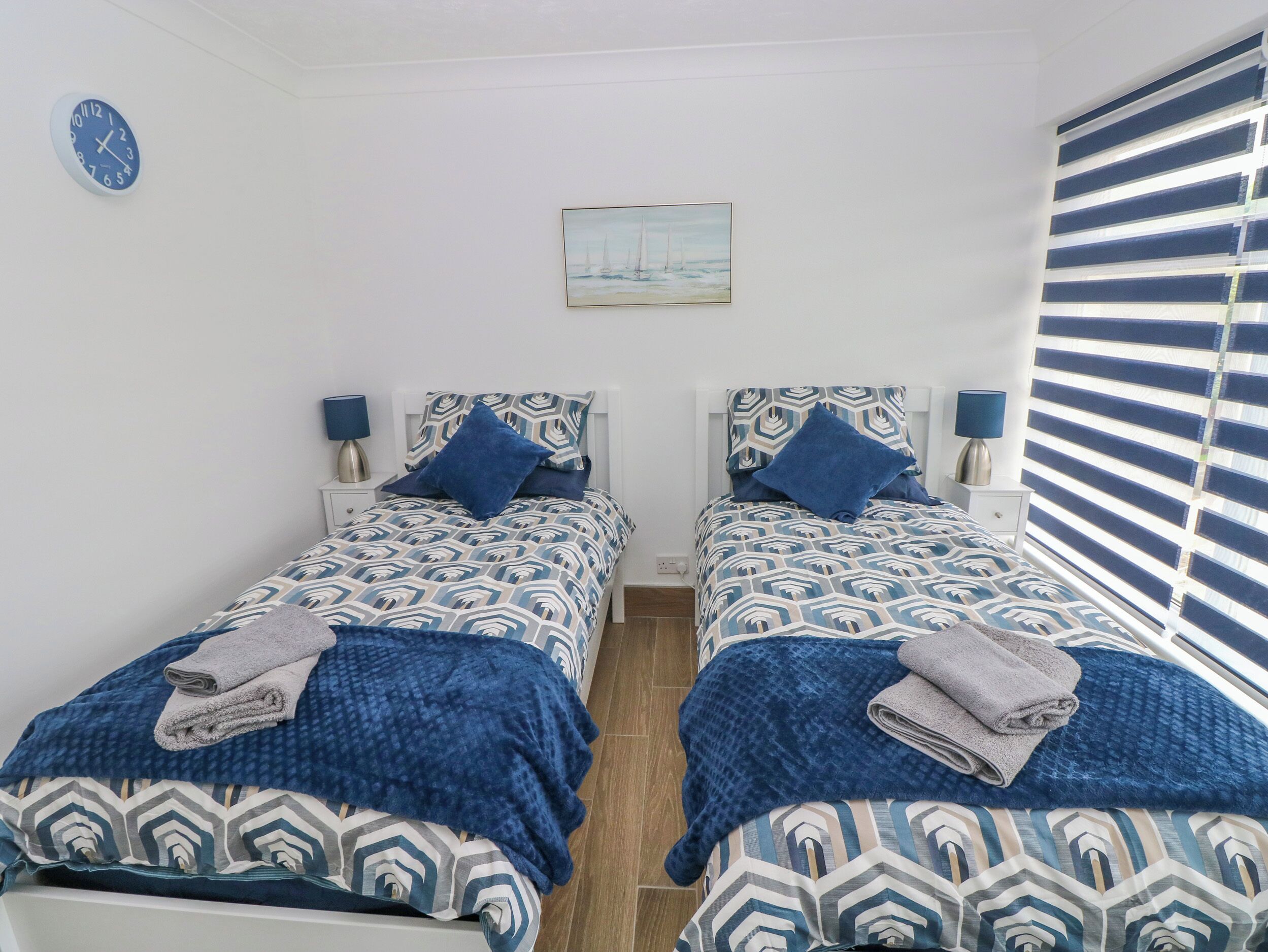 Quarto com duas camas, cada uma com roupa de cama e almofadas estampadas, um relógio na parede e um quadro sobre as camas.