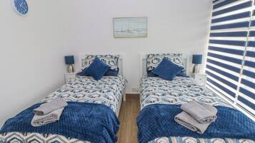 Quarto com duas camas, cada uma com roupa de cama e almofadas estampadas, um relógio na parede e um quadro sobre as camas.