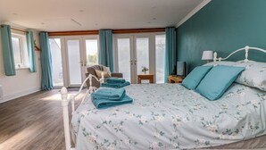 Un dormitorio con cama, una silla, una mesa y un ventanal con cortinas.