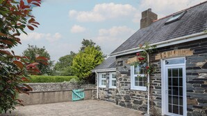 A stone building with a tiled patio, a wooden gate, and a tree in the background. - Bwthyn y Gwas (Tywyn)