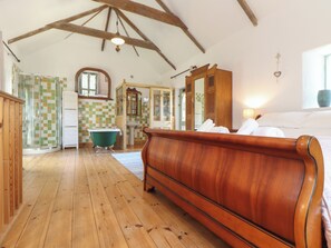 Una habitación amplia con suelo de madera, una cama grande de madera, una bañera antigua y un baño con pared de azulejos y armarios de madera.