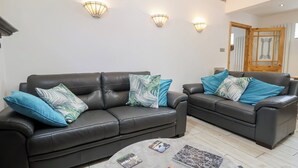 A modern living room with two black leather sofas, each with teal and white patterned cushions, and three wall-mounted light fixtures. - The Stables (Chester)