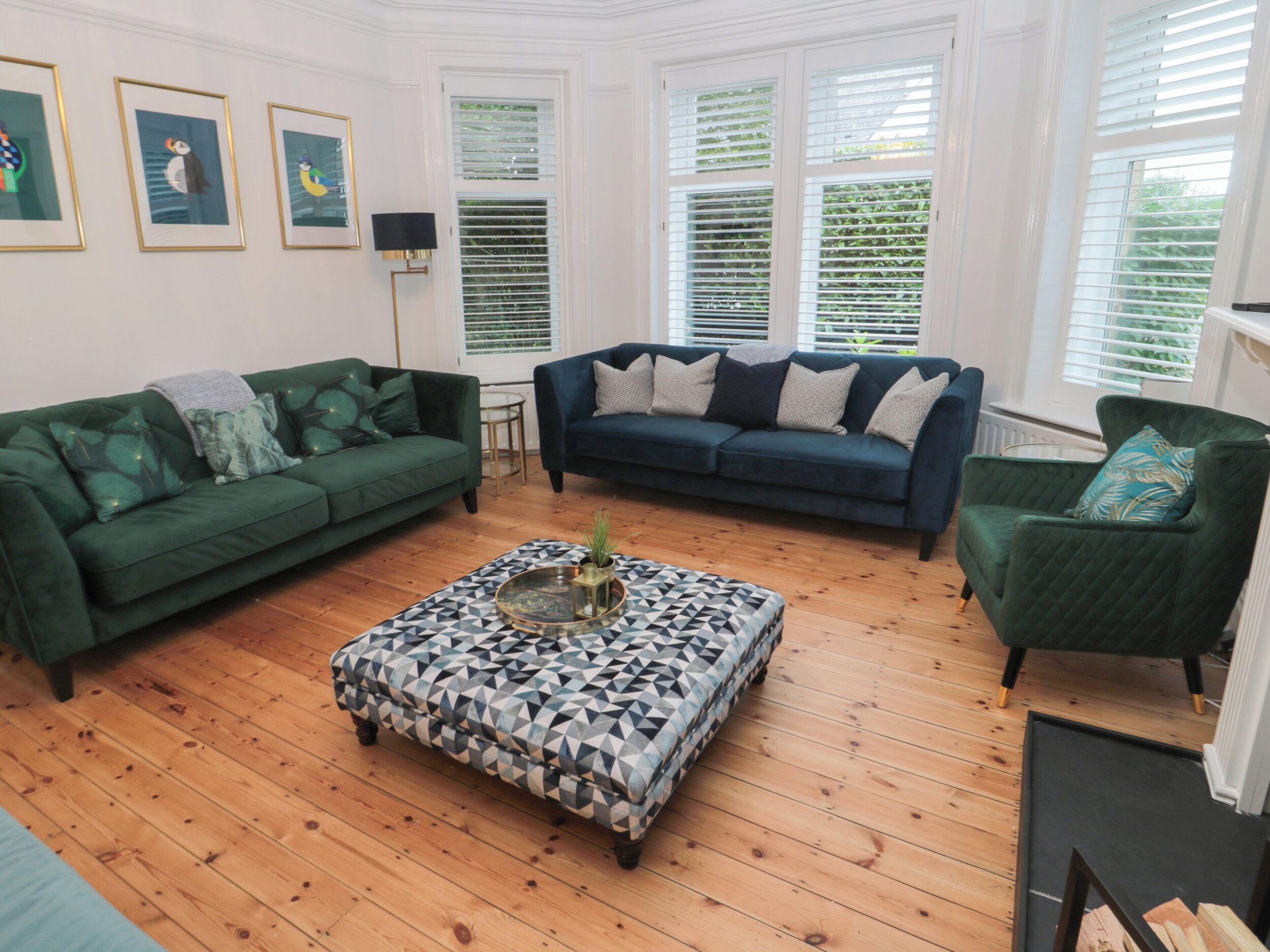 Sala de estar com dois sofás verdes, um banquinho estampado e uma poltrona verde.