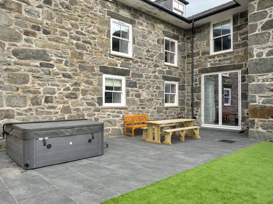 Edificio de piedra con un patio que incluye una mesa, sillas, una parrilla y una puerta corrediza de vidrio.