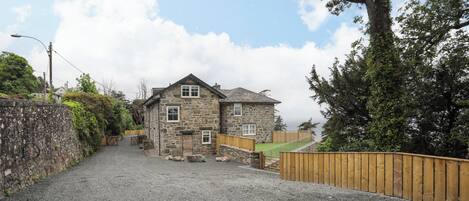 A stone house with a gravel driveway and a wooden fence.