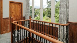 A wooden staircase with a balustrade leading to a room with large windows. - The Coach House (Dawlish)