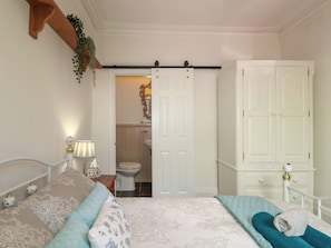 A bedroom with two beds, a white wardrobe, and a bathroom visible through an open door. - The Coach House (Dawlish)