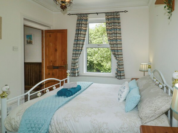 A bedroom with a bed, a window with curtains, a bedside lamp, and a door.
