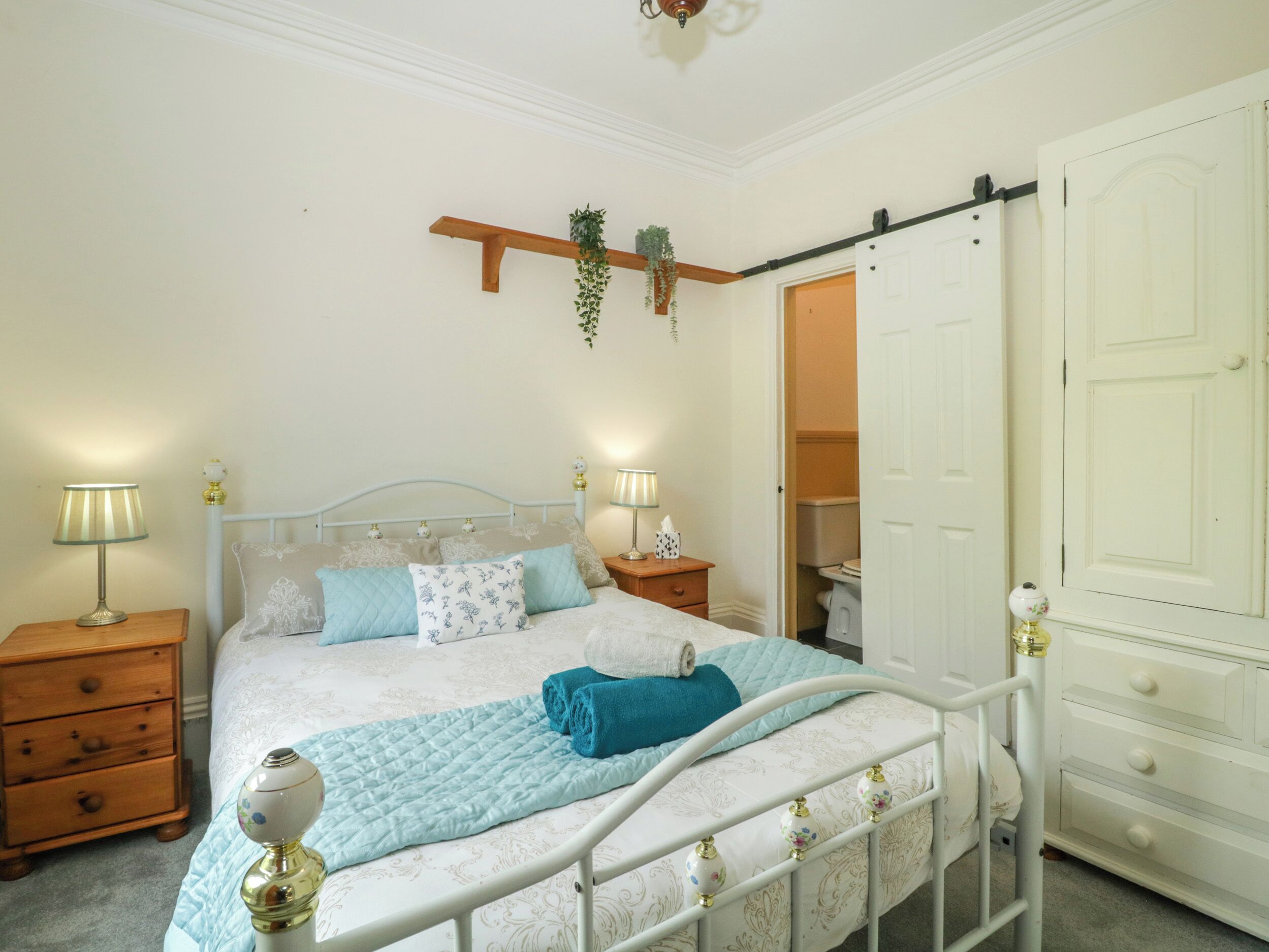 A neatly arranged bedroom with a bed, bedside tables, a dresser, and a hanging plant.