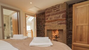 A bedroom with a stone fireplace, a wooden wardrobe, and a bed with white and beige bedding. - Heather's Cottage (Carlisle)