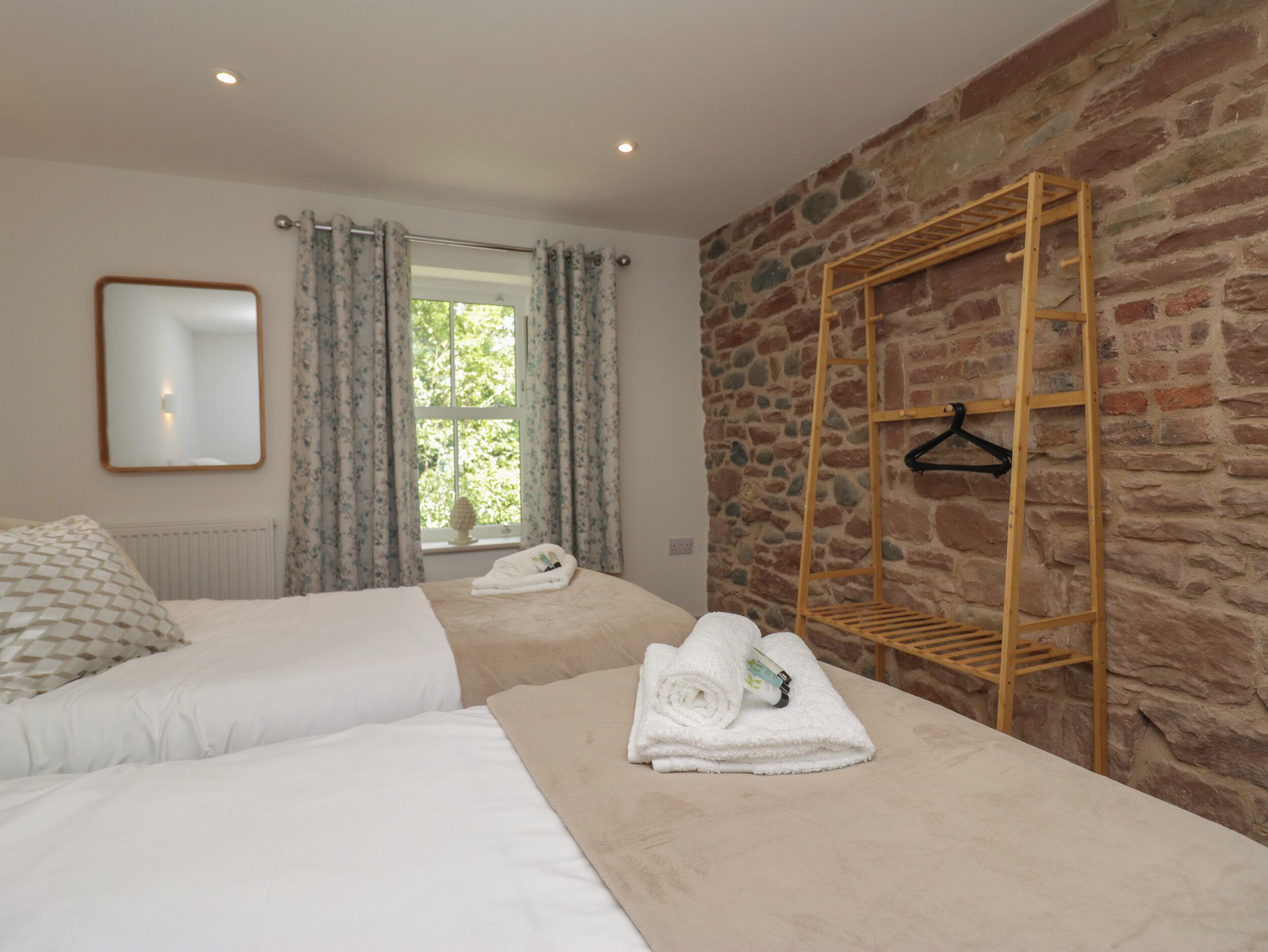 A hotel room with two beds, a stone wall, a wooden drying rack, and a window with curtains.