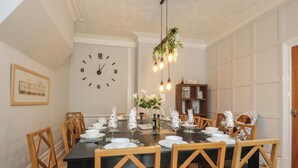 A dining room with a large clock, wooden chairs, a black table, and a hanging light fixture. - Verdo House (Blackpool)