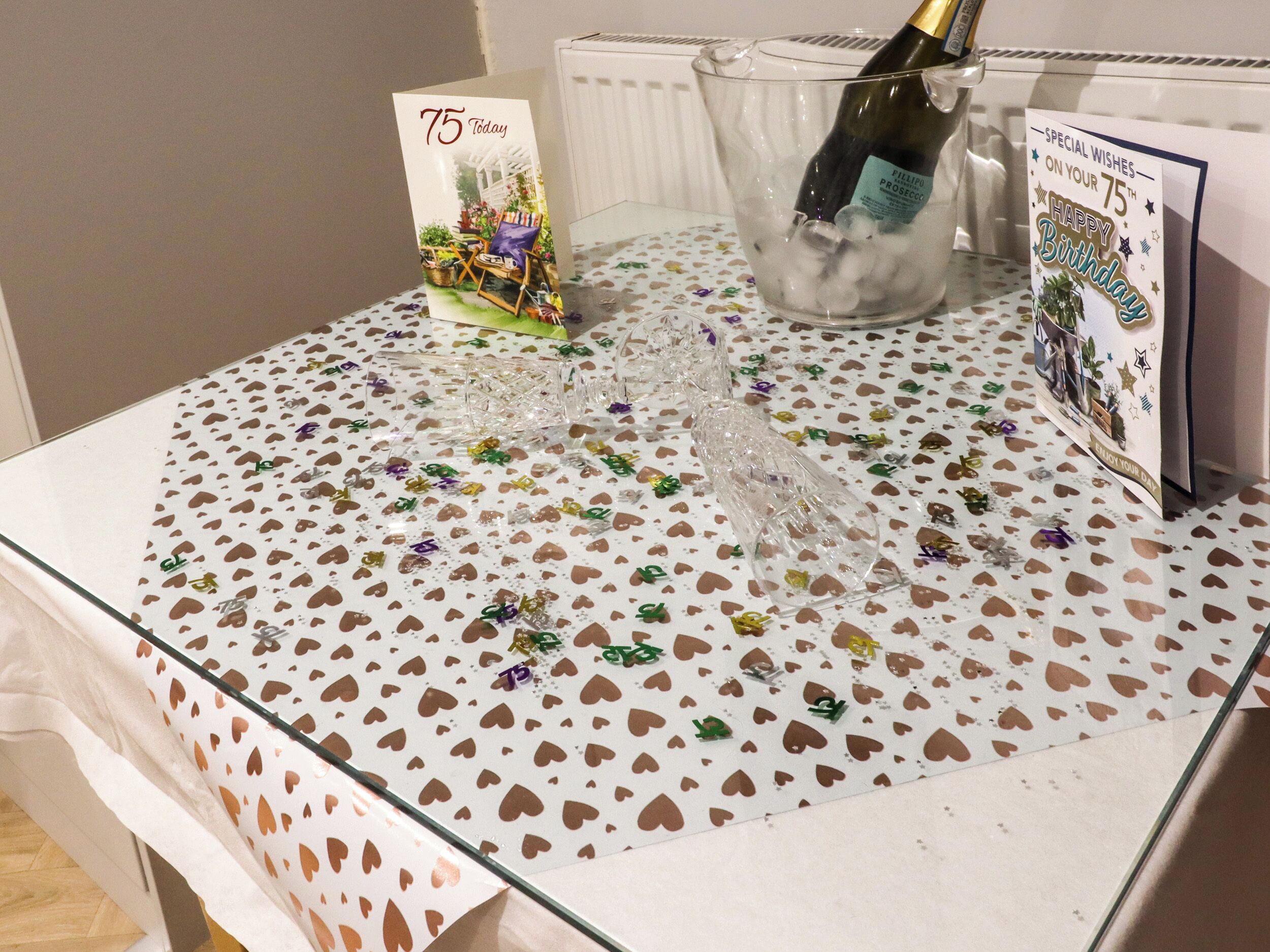 A table with a glass top, decorated with a heart-patterned tablecloth and clear glassware.