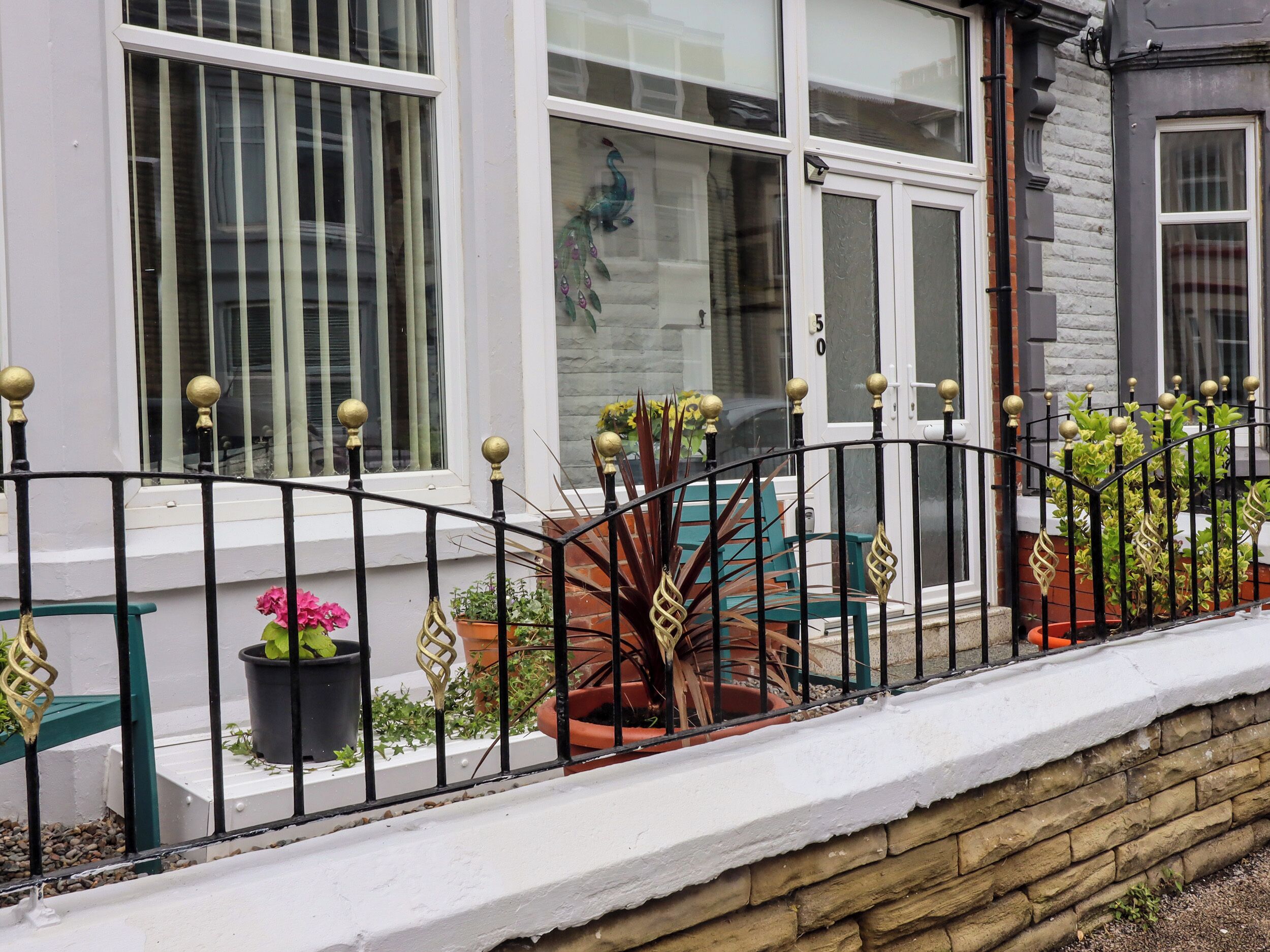 A balcony with a stone wall, potted plants, and a metal railing with decorative elements.