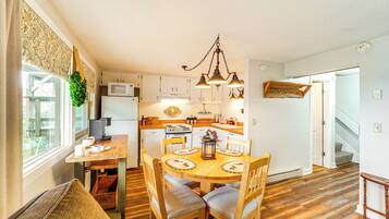 A kitchen with wooden cabinets, a dining table with chairs, a coffee maker, and a hanging light fixture.