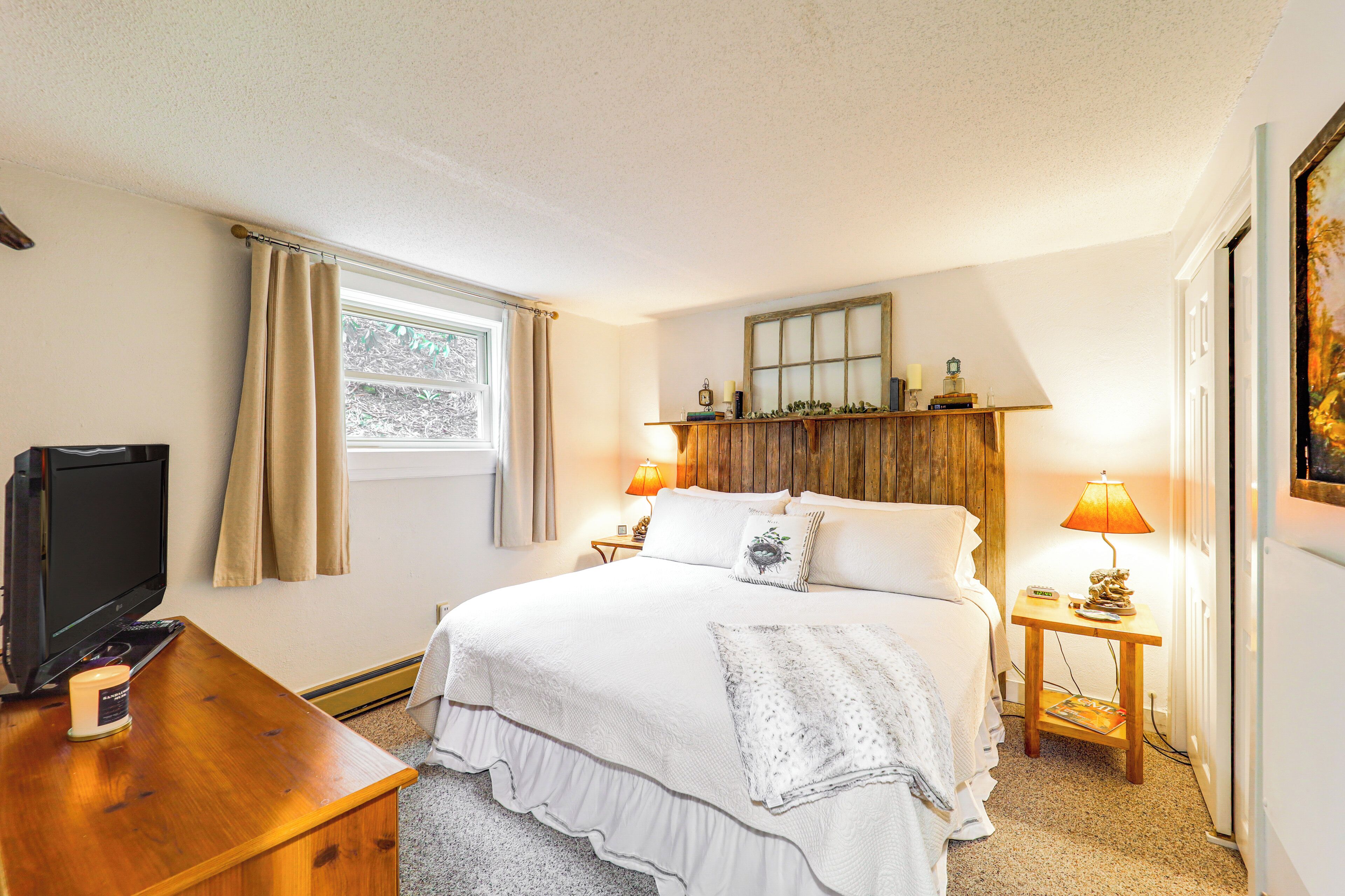 Une chambre à coucher avec un lit, des lampes de chevet, une télévision et une fenêtre avec des rideaux.
