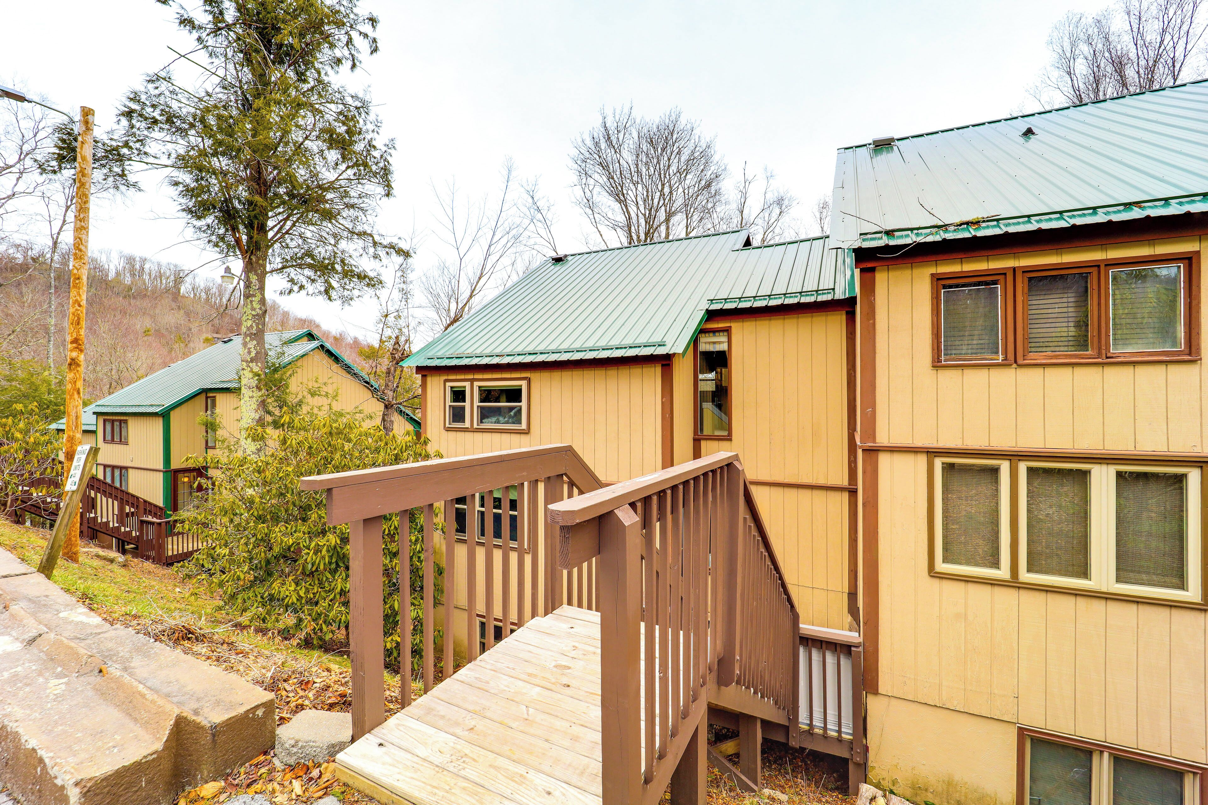 A wooden cabin with a green roof, a wooden deck, and a small porch.