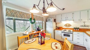 A kitchen with white cabinets, a wooden dining table with placemats, a chandelier, and a window with a wreath. - Hike, Sip & Stay Awhile! Sugar Mountain Getaway (Banner Elk)
