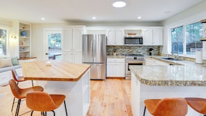 A modern kitchen with white cabinets, stainless steel appliances, and a wooden island with bar stools.
