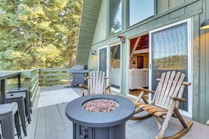 Una terraza de madera con un brasero, mobiliario exterior y un ventanal corredera que da a un espacio interior.
