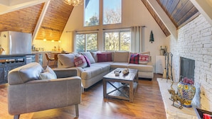 A spacious living area with a wooden ceiling, a fireplace, and a large window. - Family-friendly Lake Arrowhead Cabin w/ Game Room! (Lake Arrowhead)