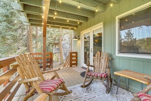 A wooden deck with rocking chairs and a bench, overlooking a forested area. - Family-friendly Lake Arrowhead Cabin w/ Game Room! (Lake Arrowhead)