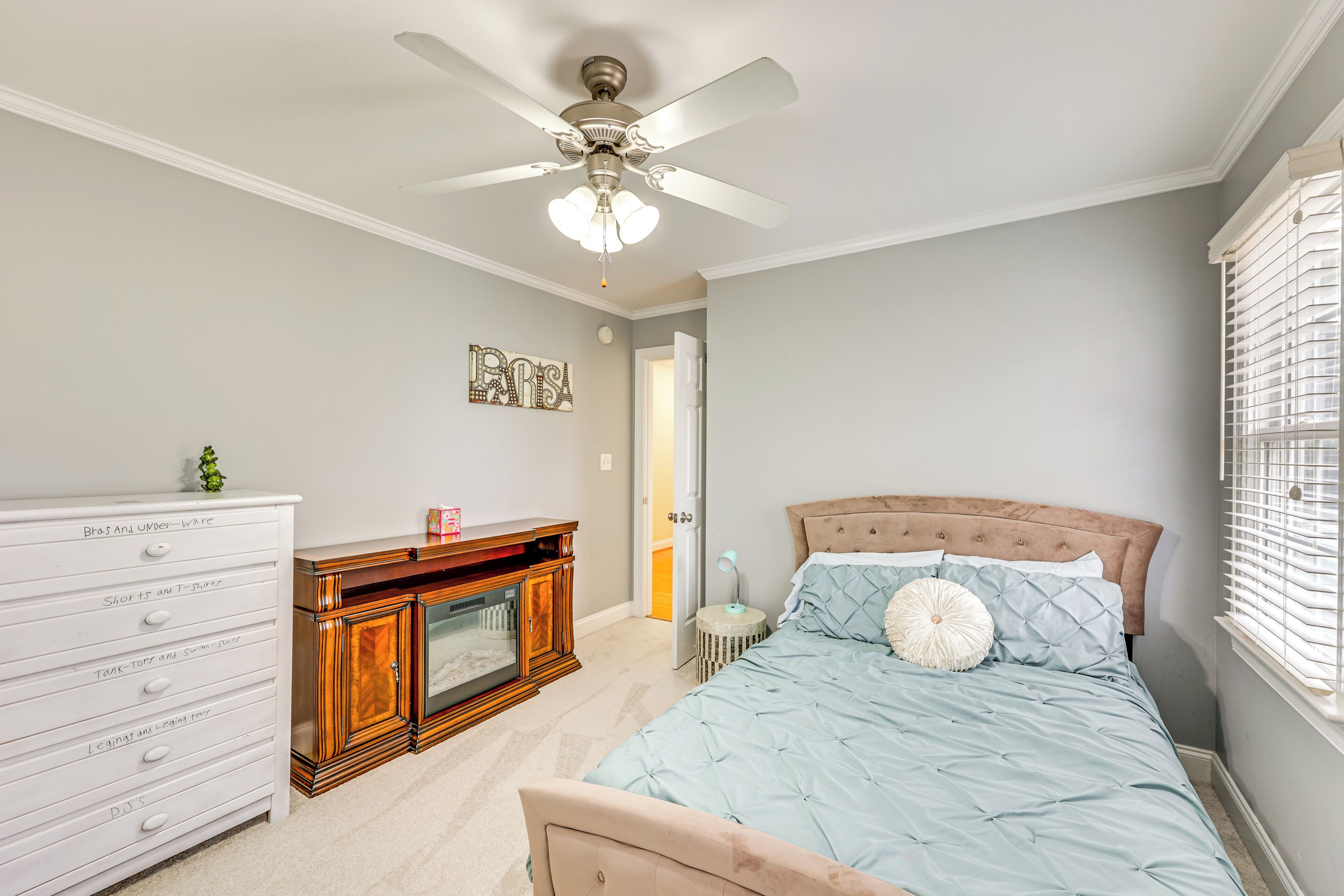 Un dormitorio con cama, cómoda, tocador y ventilador de techo.