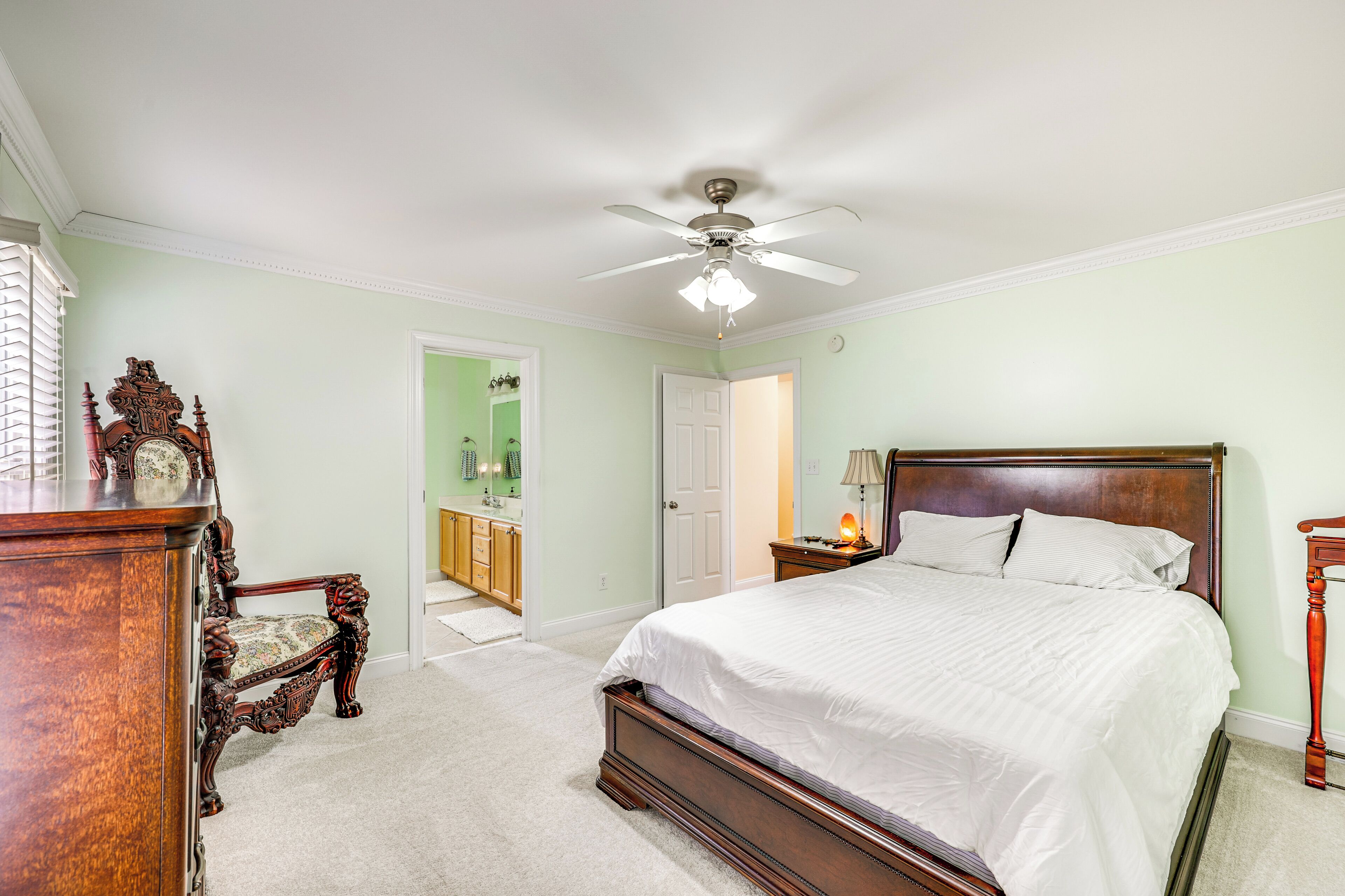 A bedroom with a large bed, a wooden dresser, a chair, and a ceiling fan.