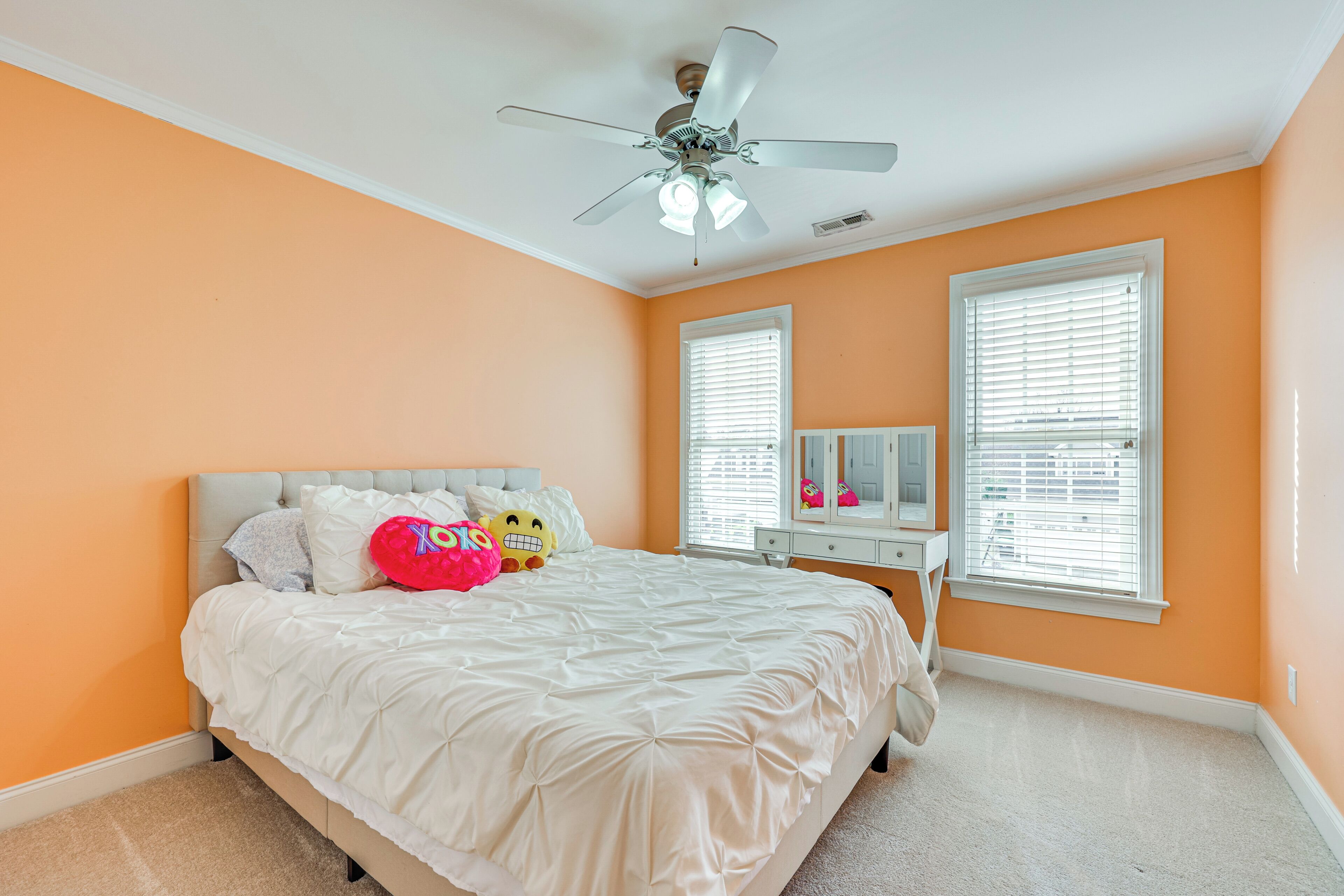 A bedroom with a bed, a ceiling fan, two windows with blinds, and a dresser.