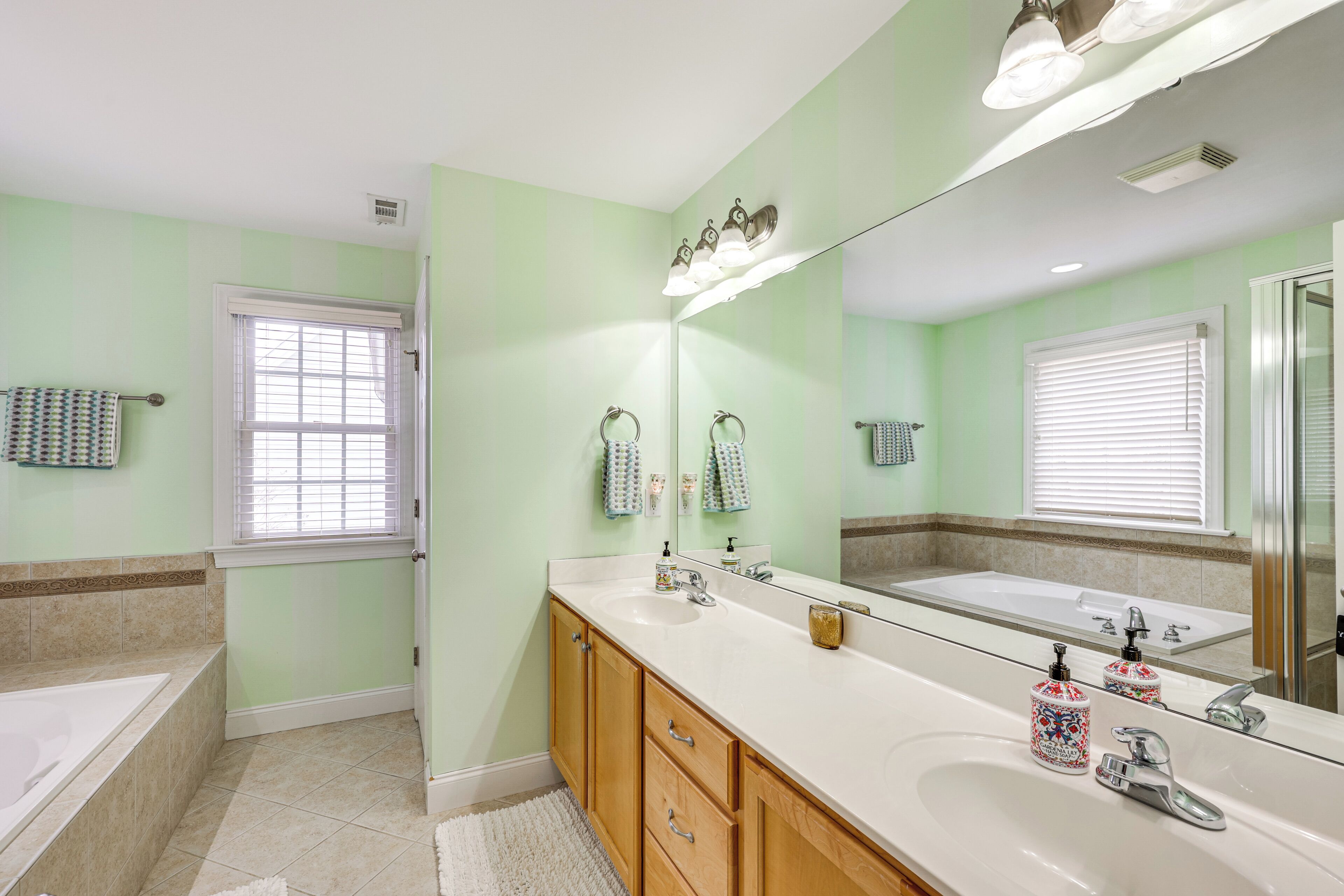 A bathroom with a large mirror, a bathtub, a sink, and a vanity with drawers.