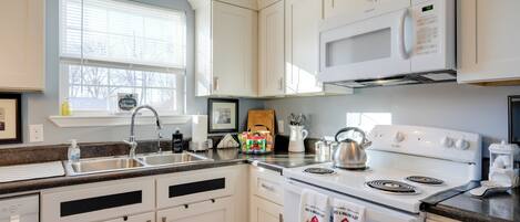 A modern kitchen with white cabinets, a stainless steel sink, a microwave, and a stove.