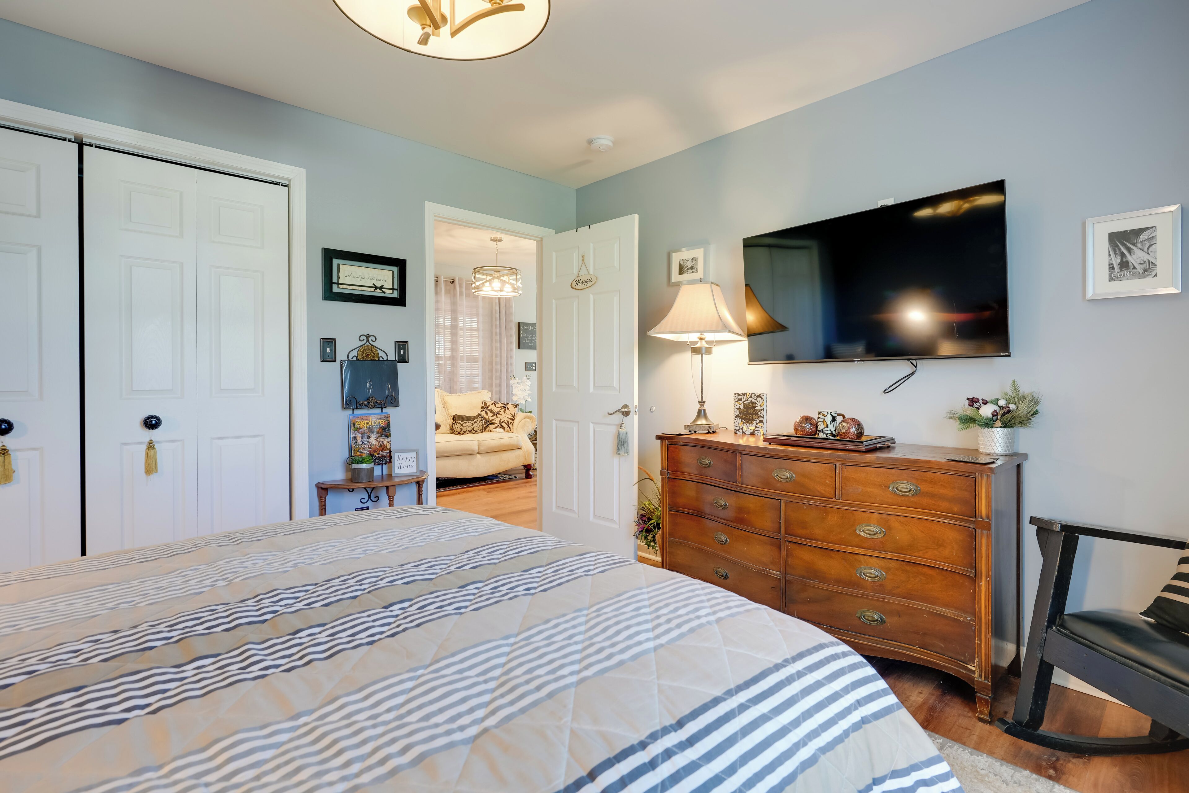 A bedroom with a large bed, a dresser, a television, and a door leading to another room.