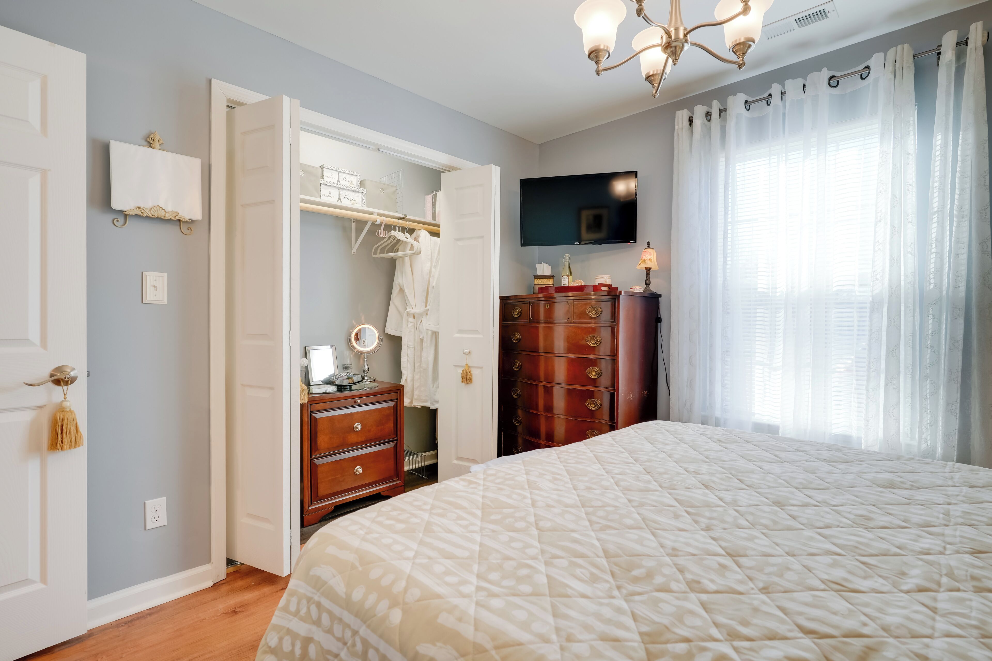 Une chambre à coucher comprenant un lit, une commode, une coiffeuse avec un miroir, un téléviseur fixé au mur et un placard avec une tringle pour suspendre les vêtements.